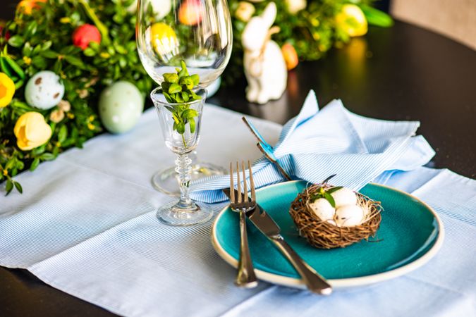 Spring table setting with bird's nest on teal plate with leafy centerpiece