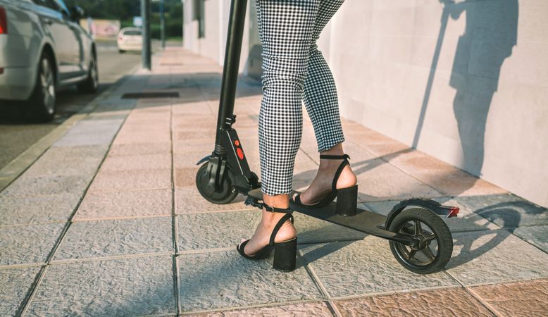 Unrecognizable businesswoman legs with e-scooter outdoors