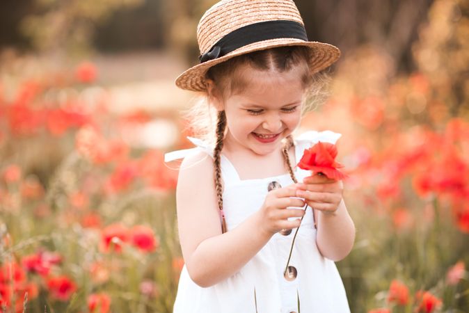 Happy girl holding red poppy flower in meadow outdoor