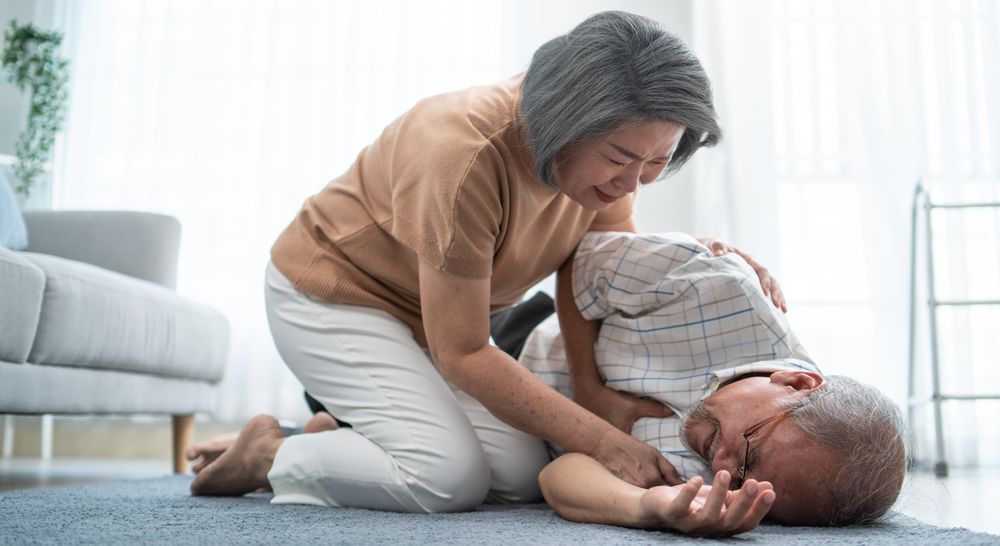 Woman helping older male patient lying on ground after falling over