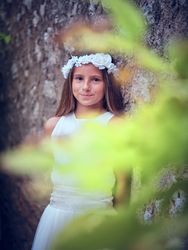 Smiling girl in white flower wreath standing near tree