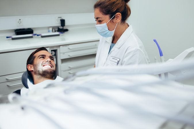 Dental doctor talking with a smiling male patient lying in dentist chair