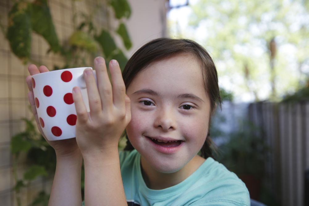 Little girl holding a white cup with red polka dots smiling at camera in backyard