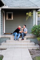 Happy family sitting on front porch with dog kissing one of the men