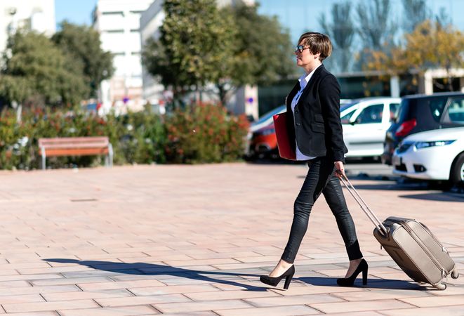 Female walking confidently outside with roller suitcase behind her