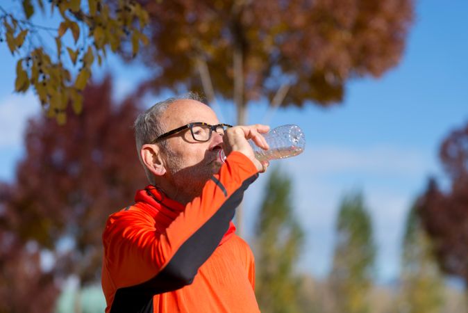 Side view of older man drinking from water bottle in park in autumn