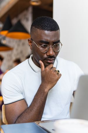 Serious Black man using laptop at table in cafe