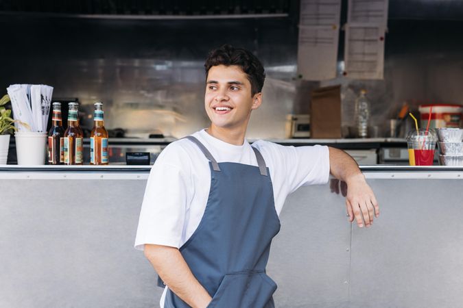 Male in apron smiling while leaning on open counter of food truck