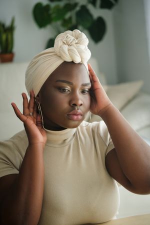 Black female touching headscarf and looking in mirror