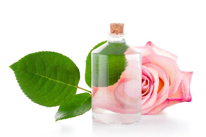 Rose water bottle on bright background with rose and leaves