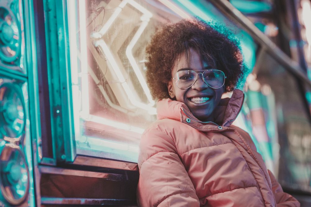 Cheerful Black woman near neon sign