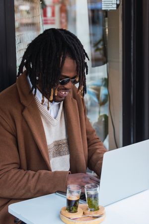 Happy Black man browsing on laptop on restaurant terrace