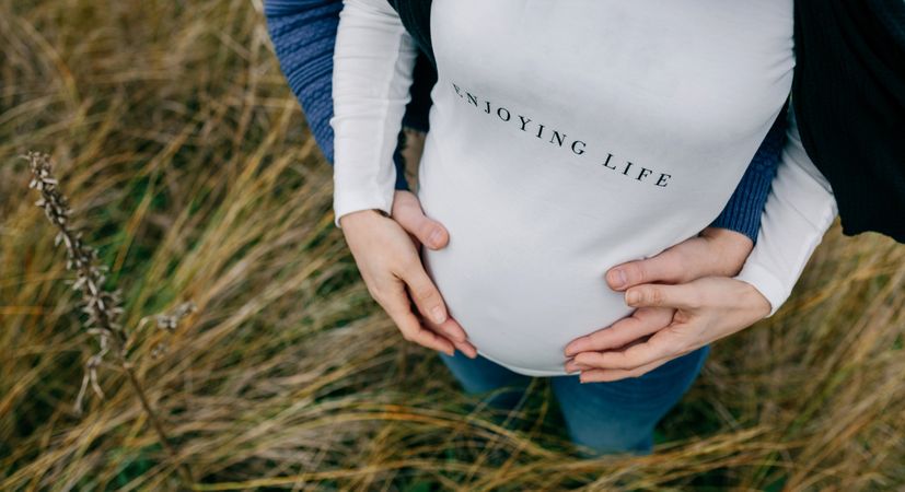 Pregnant woman with partner hugging and holding belly