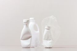 Three crushed plastic bottles and cup on neutral background