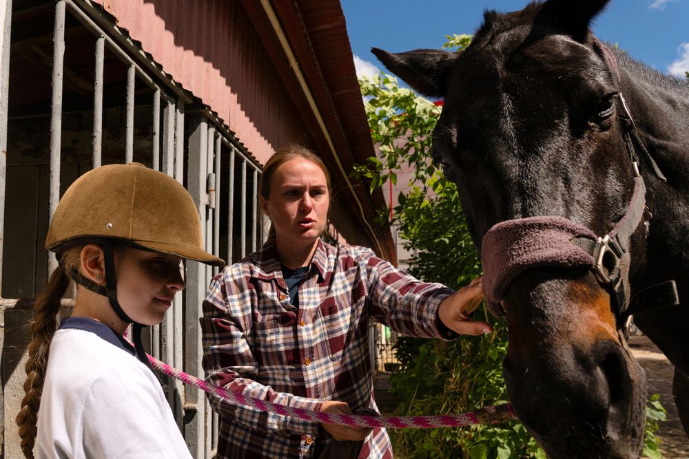Instructor points to horse while girl holds lead rope.
