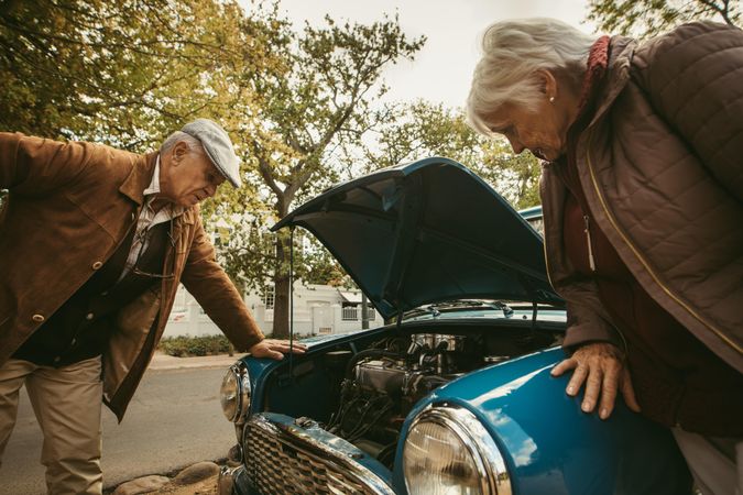 Mature man and mature woman looking at the engine of broken car