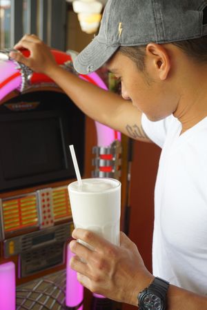 Man holding a cup of milkshake standing beside pink jukebox