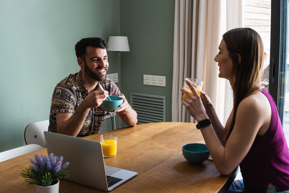 Happy friend having lunch and using laptop on dining table