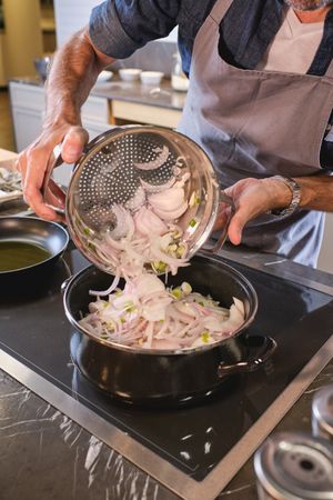Unrecognizable man pouring chopped onion into frying pan