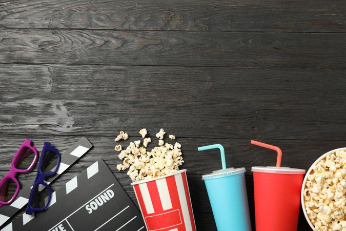 Flat lay. Buckets with popcorn, clapperboard, 3d glasses and drinks on wood background
