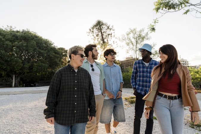 Group of diverse young friends walking together outdoors at sunset in casual style