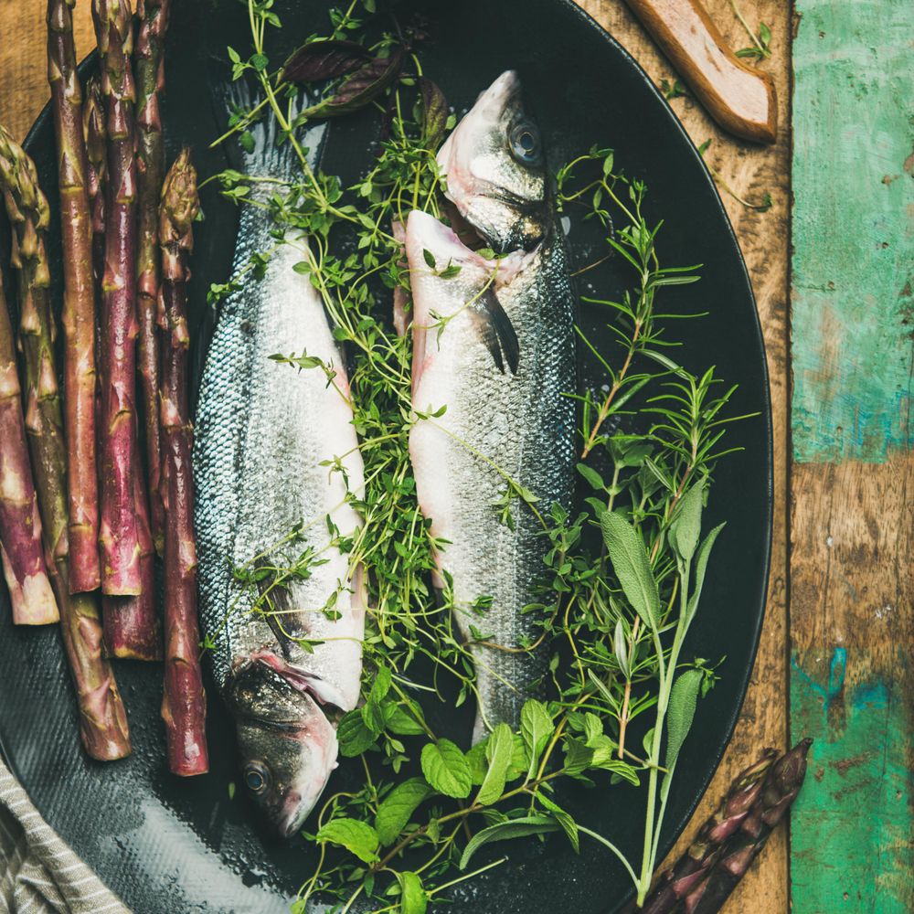 Sea bass with herbs and purple asparagus in dark bowl, square crop