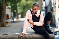 Calm male sitting in city texting on phone