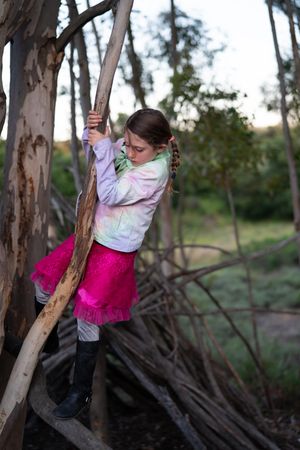 Girl in tie-dye jacket and pink skirt climbing eucalyptus tree