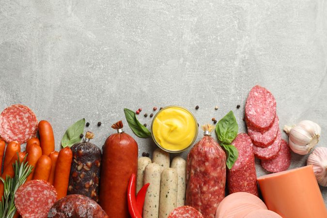 Variety of cured meats, fresh herbs and mustard on grey table with space for text