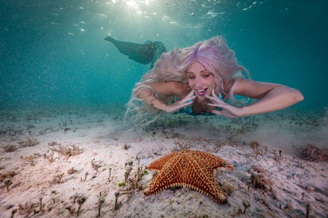 Redhead fairytale female mermaid swimming beside starfish