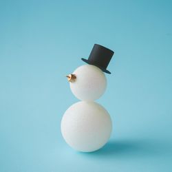 Snowman in top hat made of Christmas bauble decoration on pastel blue background