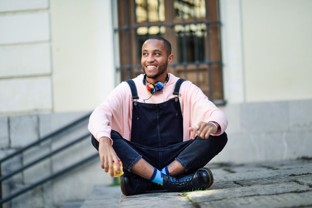 Smiling male in overalls and boots sitting cross legged on outdoor steps