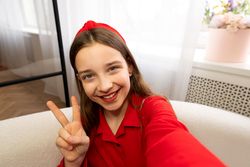 Close-up selfie of smiling teen girl showing peace gesture.