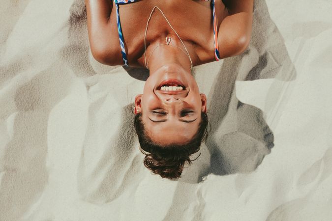 Top view of a smiling woman lying on beach sand