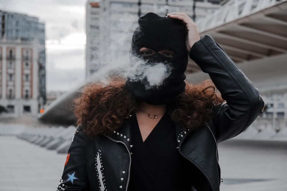 Woman in mask and jacket smoking on street