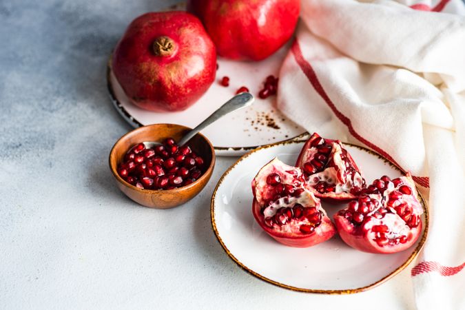 Fresh cut pomegranate on light plate with bowl of seeds with space for text