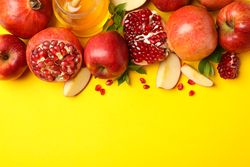 Top view of fresh apples, pomegranate and honey on yellow background with copy space