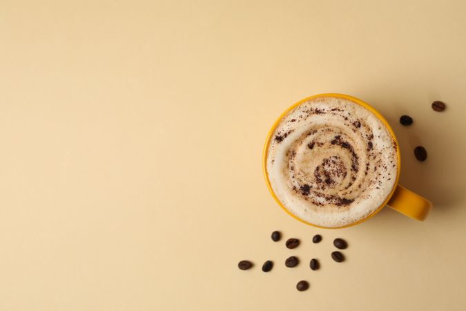 Cup of latte and coffee seeds on beige background