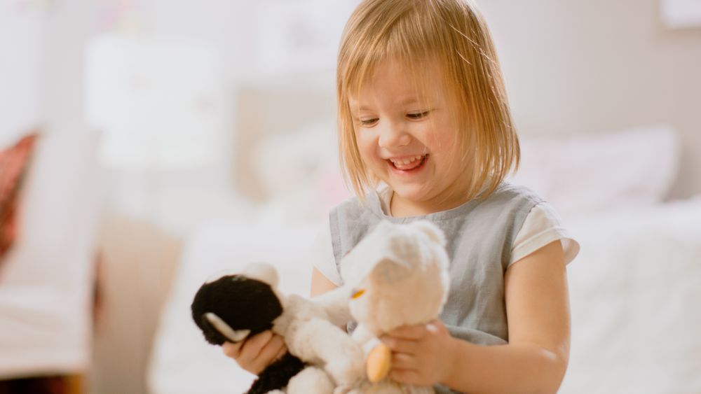 In the Children's Room: Happy Little Girl Playing with Doll House and Sitting on a Carpet.