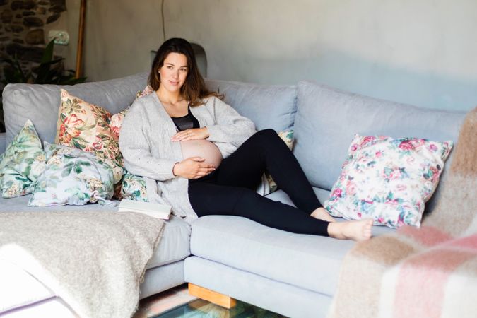 Relaxed pregnant woman holding her belly on sofa