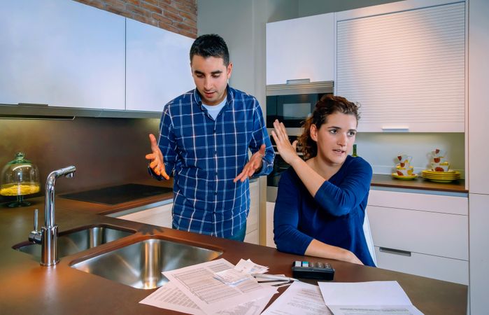Frustrated couple arguing with bills strewn on the kitchen counter