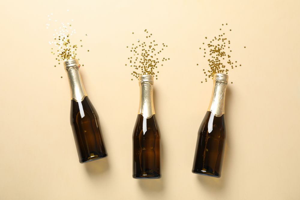 Champagne bottles and glitter on beige background, space for text