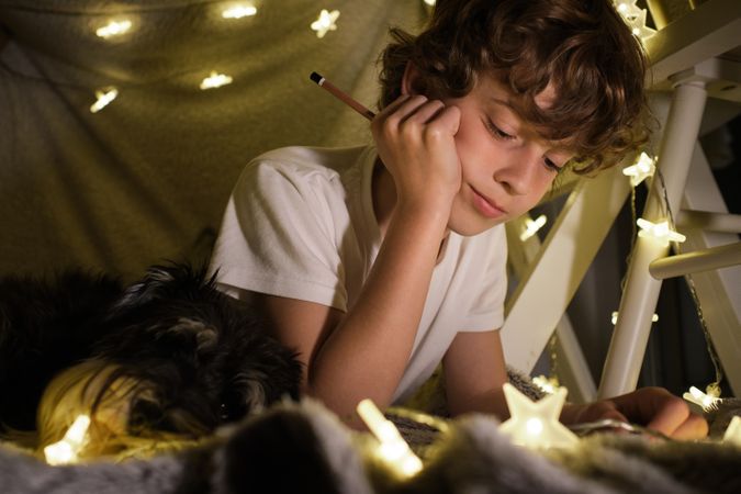 Content boy with pencil in blanket fort