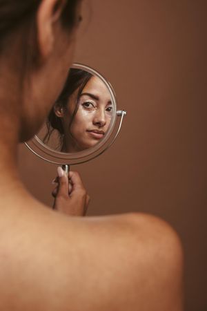 Woman with vitiligo looking at a mirror against brown background