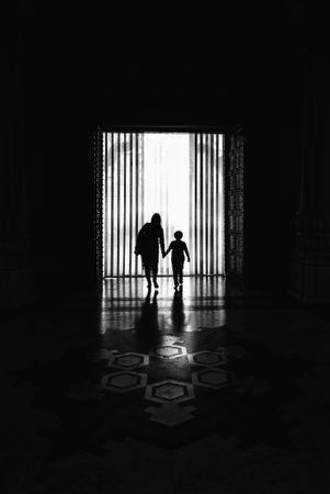Mother hold her child's hand walking in hallway in grayscale