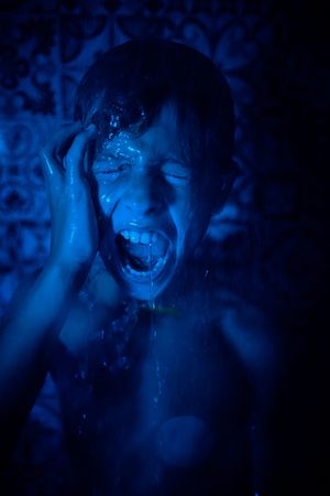 Displeased boy with water on face yelling in bathroom