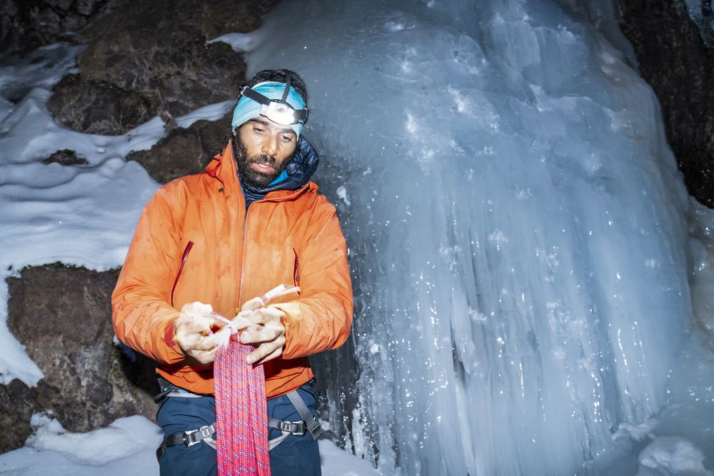 Tired climber carrying rope while standing by frozen glacier