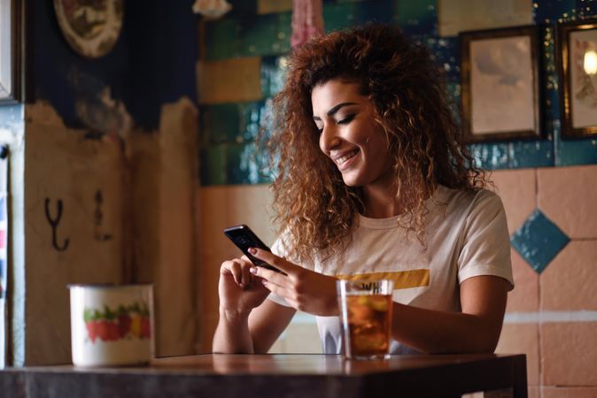 Arab woman in casual clothes texting on her phone at restaurant table