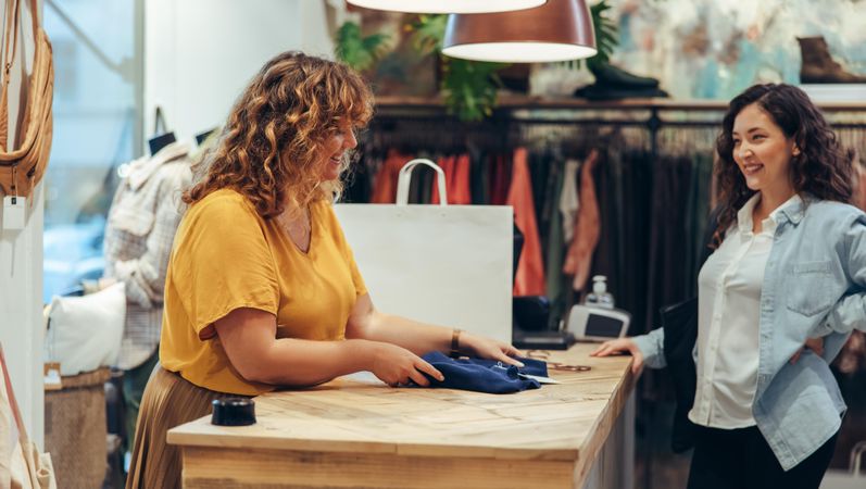 Fashion store owner folding clothes for customer at checkout counter