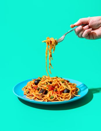Pasta puttanesca plate minimalist on a green background